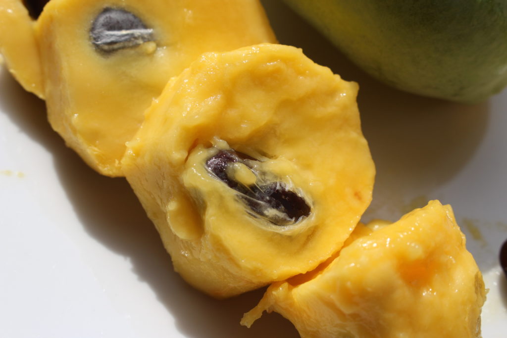 A close up of cut-up cross-sections of a pawpaw which have had the skins removed.