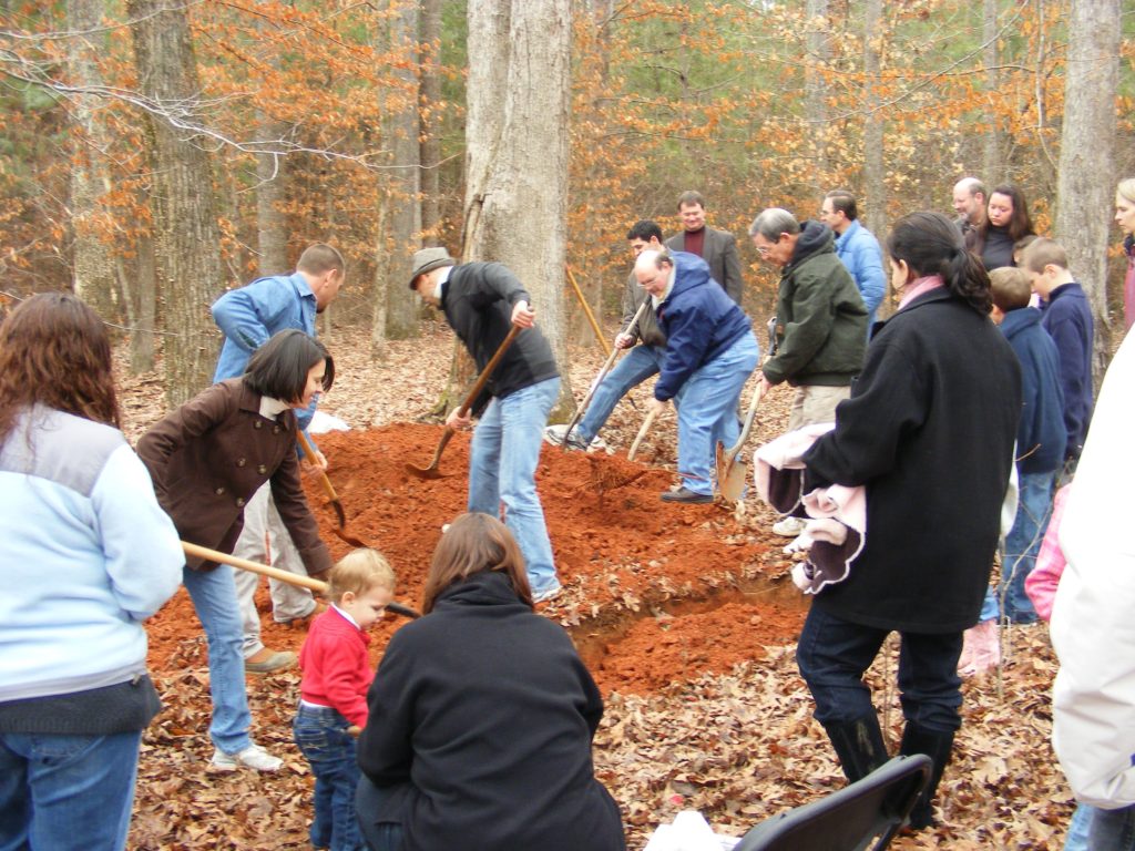 People using shovels to fill in grave in the woods