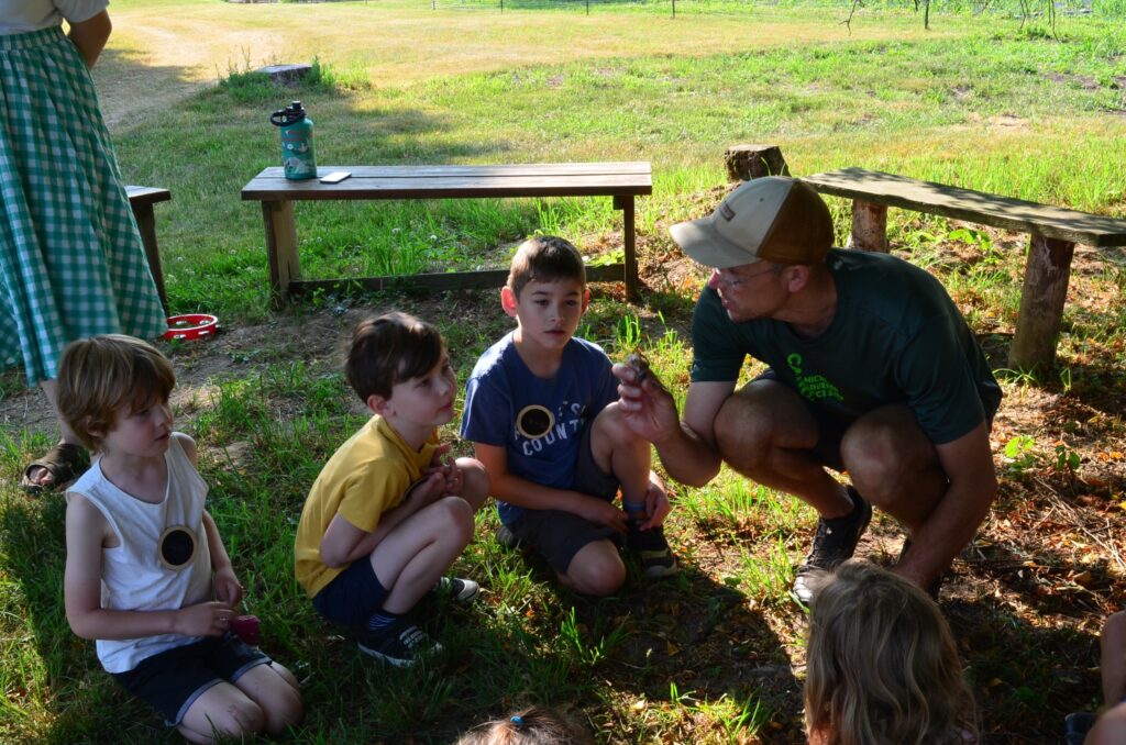 Three boys watching as farmer Mike explains a plant that he is holding.